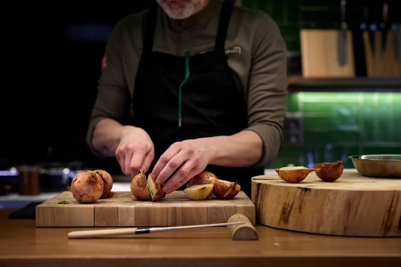 Rodrigo de la Calle corta cebollas asadas sobre la tabla de madera de la cocina
