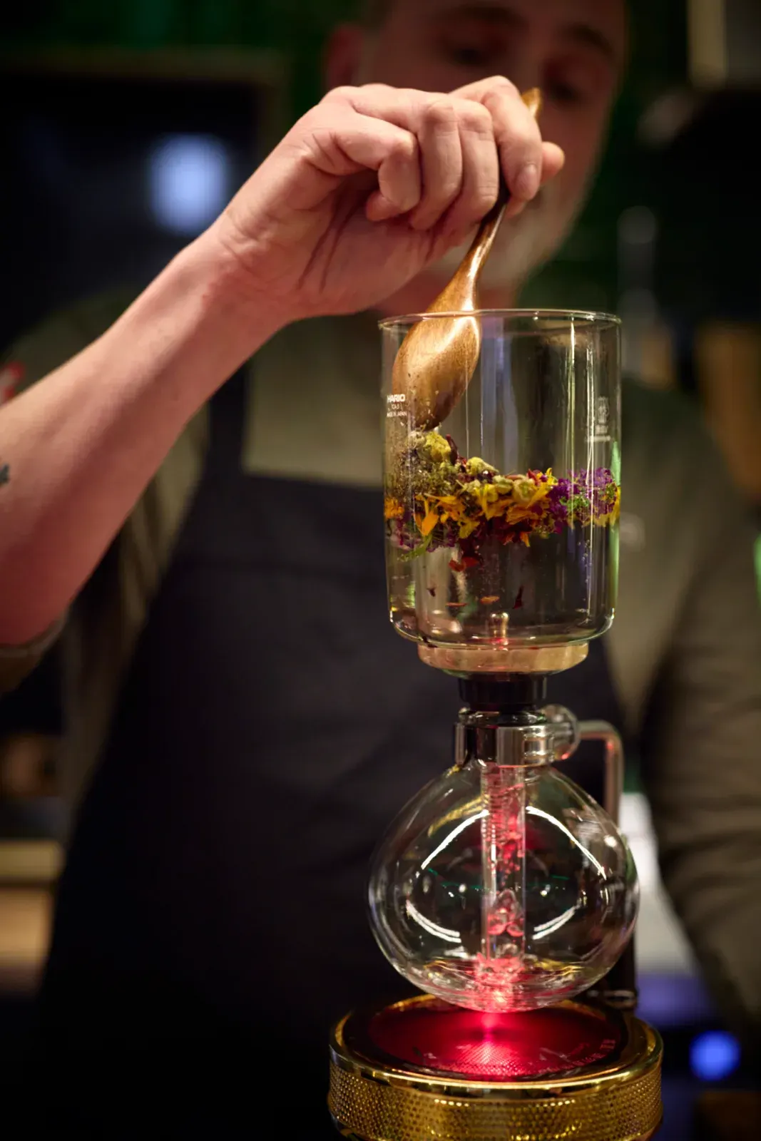 Flores y hierbas secas en la cámara de cristal del sifón, removidas con cuchara de madera antes de la extracción